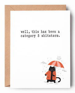Funny letterpress encouragement card for hard times, features a black cat holding an umbrella in the rain. It says: Well, this has been a Category 5 shitstorm.